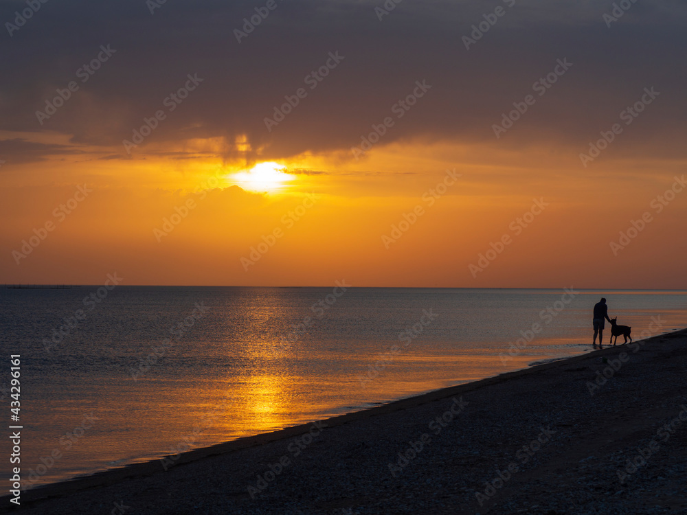 Beautiful unusual sunset on the sea, silhouettes of a girl with a dog walking along the water's edge