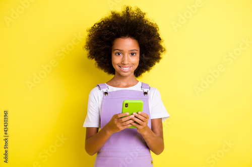 Photo of optimistic cute curly girl hold telephone wear white t-shirt violet dress isolated on yellow color background