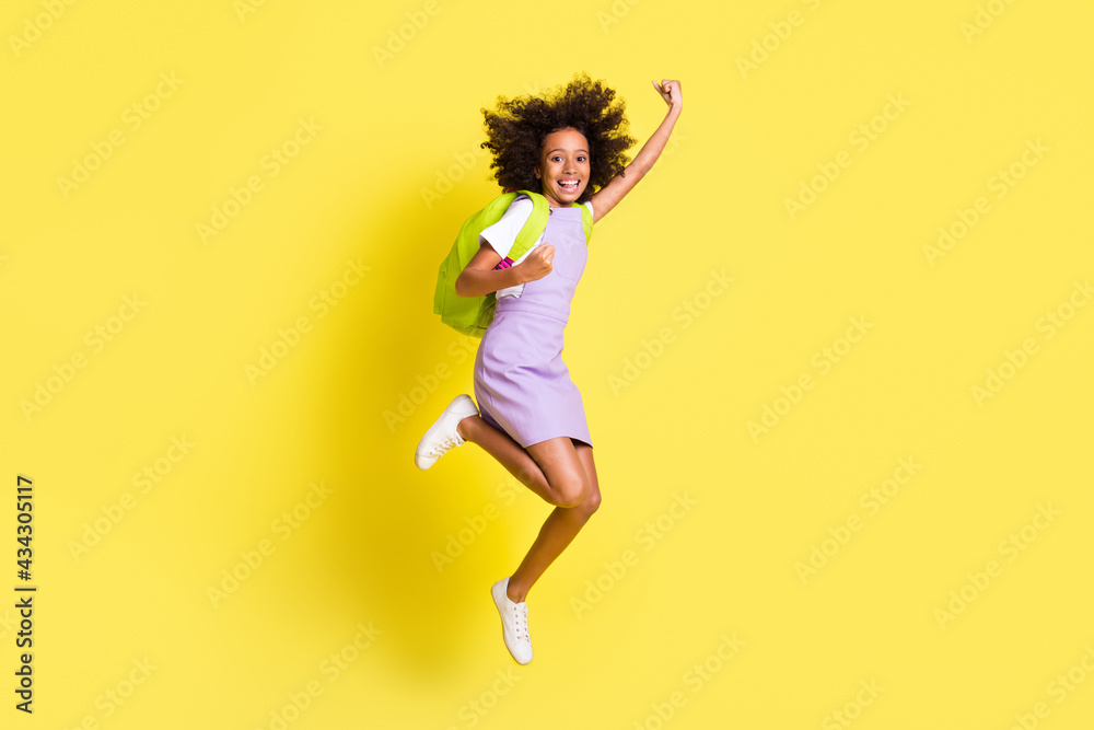Full size photo of optimistic cute curly girl jump wear rucksack t-shirt dress isolated on yellow color background Full size photo of optimistic cute curly girl jump wear rucksack t-shirt dress isolated on yellow color background