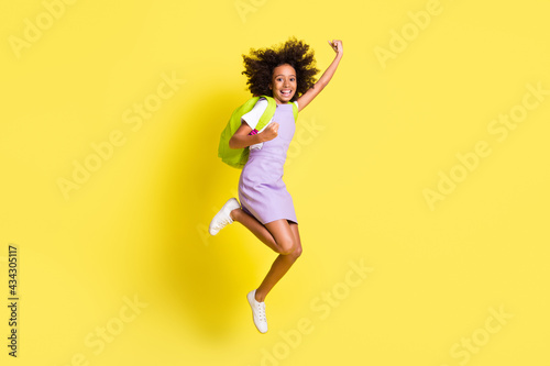 Full size photo of optimistic cute curly girl jump wear rucksack t-shirt dress isolated on yellow color background