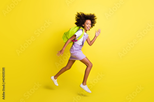 Full length body size profile side view of cheerful active wavy-haired girl jumping running isolated over vivid yellow color background
