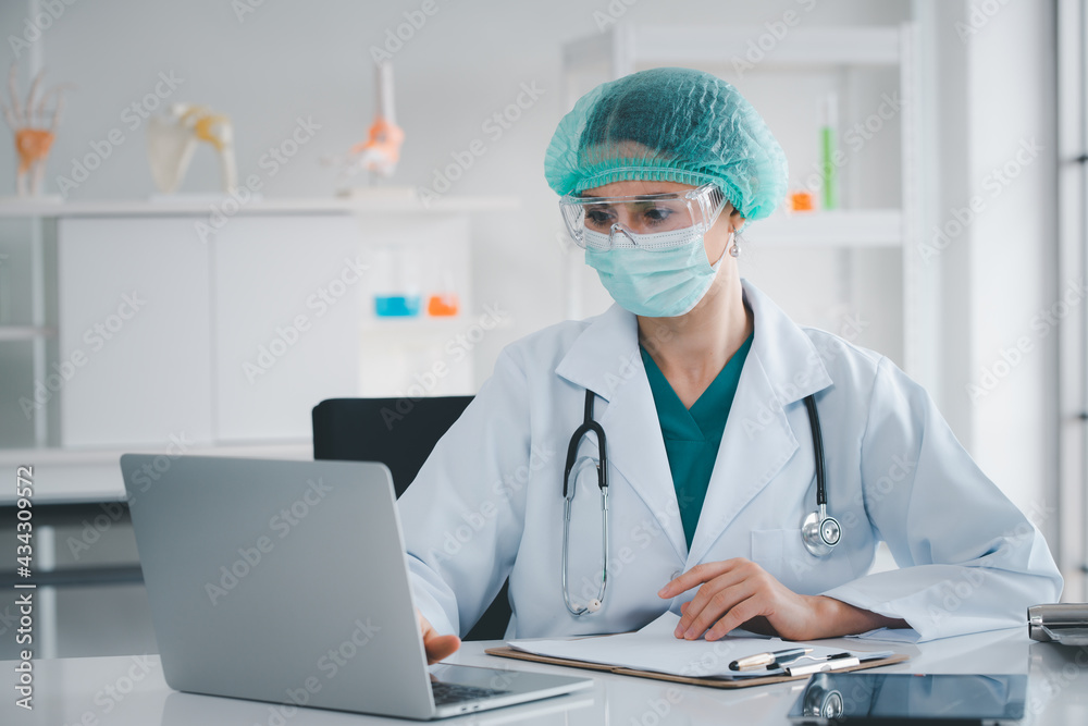 Doctor vaccine test in laboratory for treatment people ,Vaccine is concept of fight against coronavirus ,looking detail in notebook wearing mask ,medical hat and glasses healthy and medical concept. Doctor vaccine test in laboratory for treatment people ,Vaccine is concept of fight against coronavirus ,looking detail in notebook wearing mask ,medical hat and glasses healthy and medical concept.