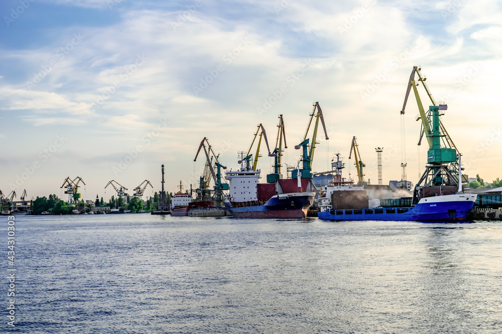 Kherson, Ukraine - July 22, 2020: View from the Dnieper river to the Kherson river port. Cargo ships moored near the shore against the background of large port cranes on a summer evening