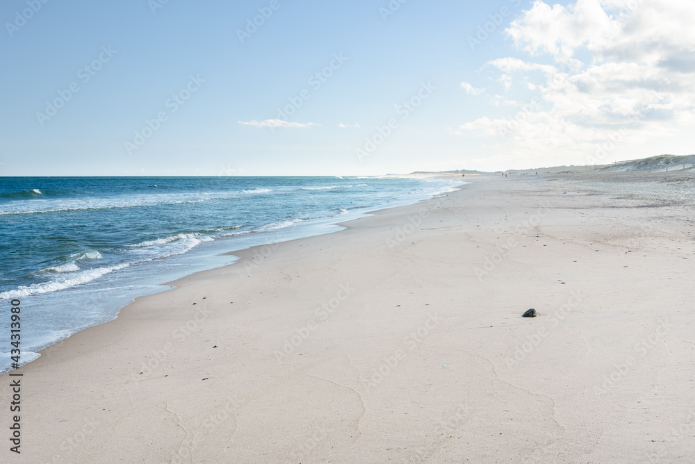 Large sandy beach backed by dunes on a clear autumn day. People strooling along the beach are visible in distance. Large sandy beach backed by dunes on a clear autumn day. People strooling along the beach are visible in distance.