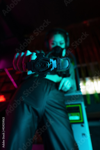 low angle view of blurred asian woman in gas mask and wireless headphones looking at camera while aiming with gun © LIGHTFIELD STUDIOS