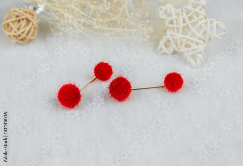 Red pompon earrings in the shape of two fluffy balls.Earrings are next to rattan products  flower specimens and other ornaments