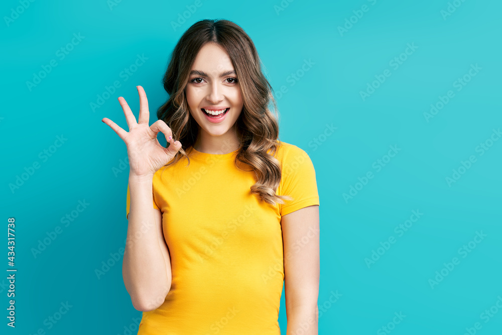 Pretty smiling woman showing OK sign with fingers over blue background Pretty smiling woman showing OK sign with fingers over blue background