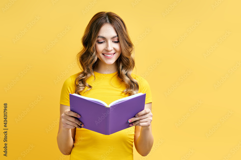 Smiling positive girl reading book on yellow background Smiling positive girl reading book on yellow background