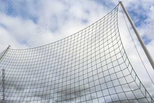 Detail eines Ballfangnetzes an einer Sportanlage vor blauem Himmel und Wolken
