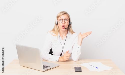 blonde pretty woman young blonde woman looking surprised and shocked, with jaw dropped holding an object and working with a laptop photo