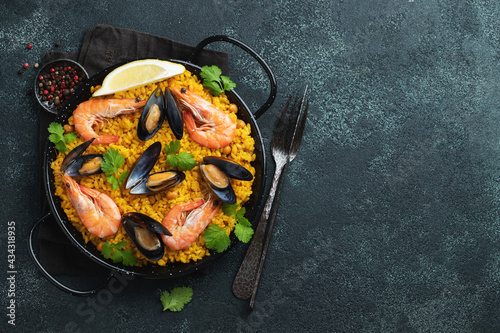 Traditional spanish seafood paella in pan with chickpeas, shrimps, mussels, squid on black concrete background. Top view with copy space