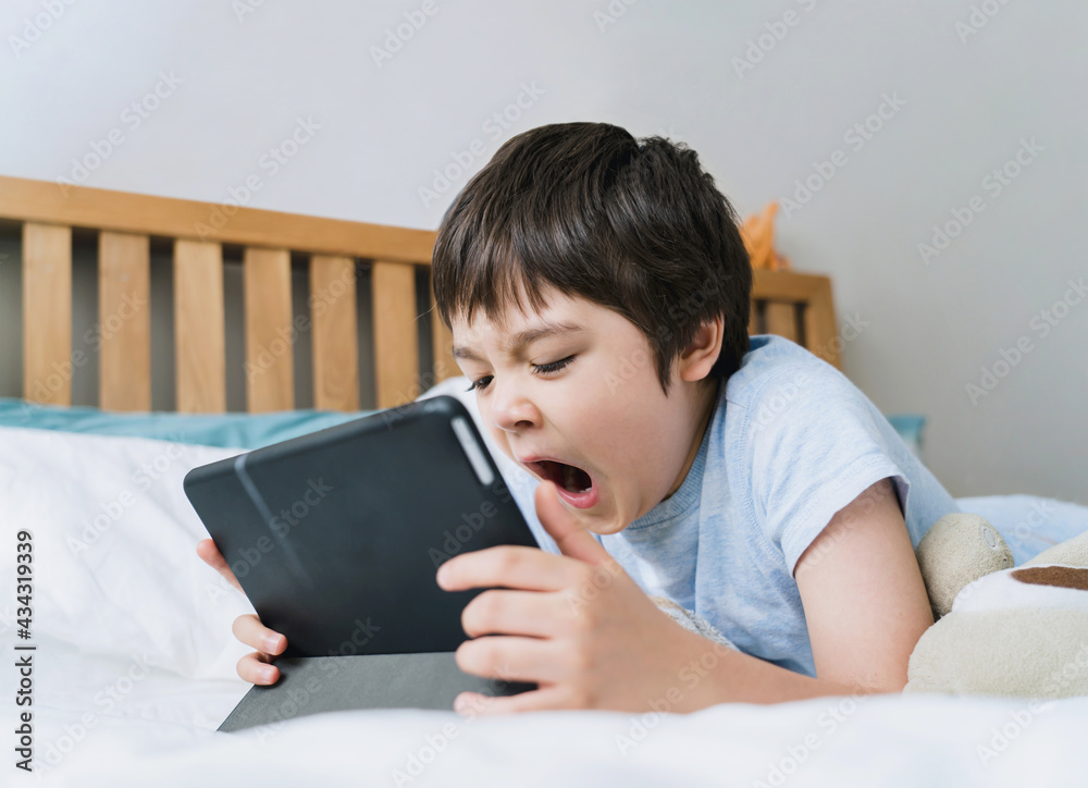 Portrait sleepy boy yawning while watching cartoon or play games on tablet, Tired kid lying in bed in morning, Cute little boy relaxing or having a nap in bed room. Children Health care concept Portrait sleepy boy yawning while watching cartoon or play games on tablet, Tired kid lying in bed in morning, Cute little boy relaxing or having a nap in bed room. Children Health care concept