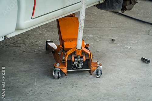 Fototapeta Naklejka Na Ścianę i Meble -  Car Lifted With Orange Hydraulic Floor Jack For Repairing or Change tire