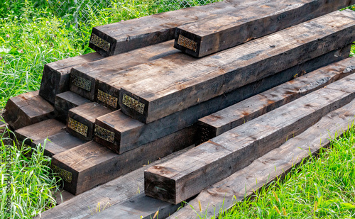 New railway sleepers impregnated with cryosote lie on green grass stacked on top of each other.