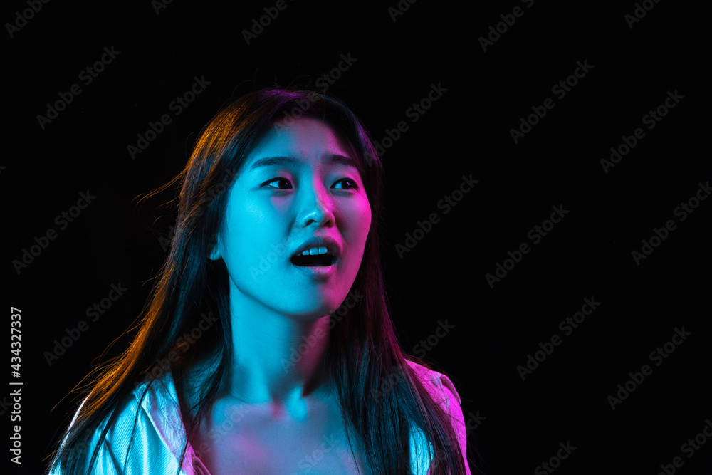 Fototapeta premium Asian young woman's portrait on dark studio background in neon. Concept of human emotions, facial expression, youth, sales, ad.