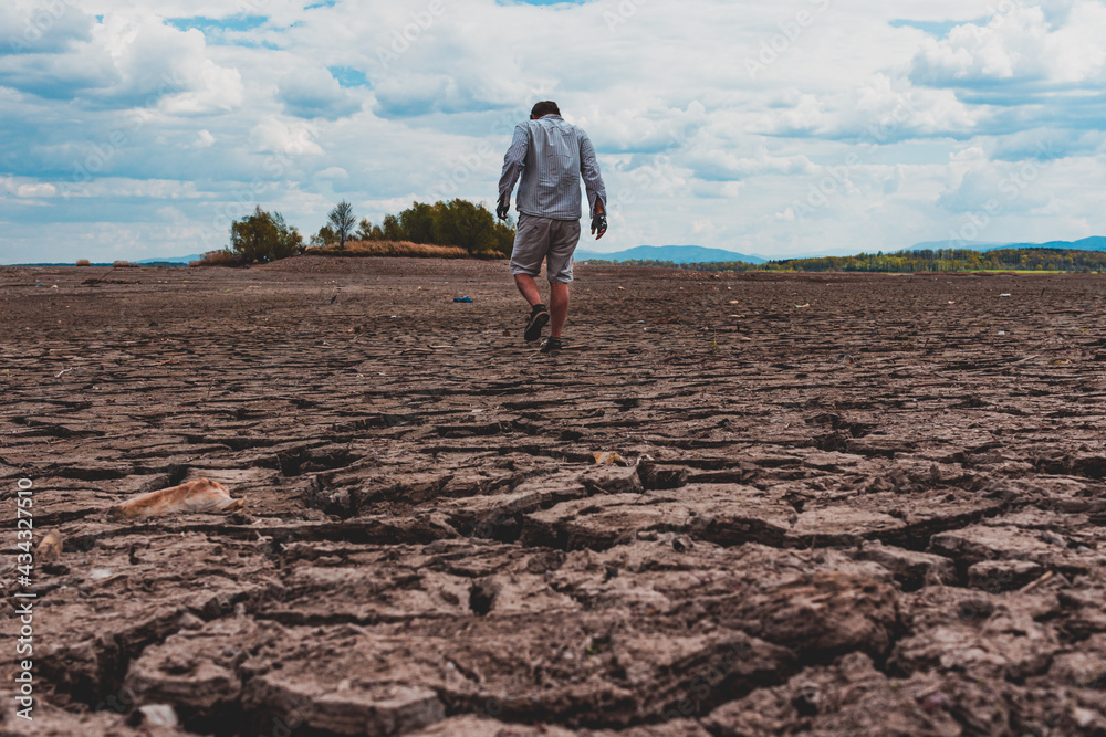 Obraz premium Man walking at cracked earth at the bottom dried up lake