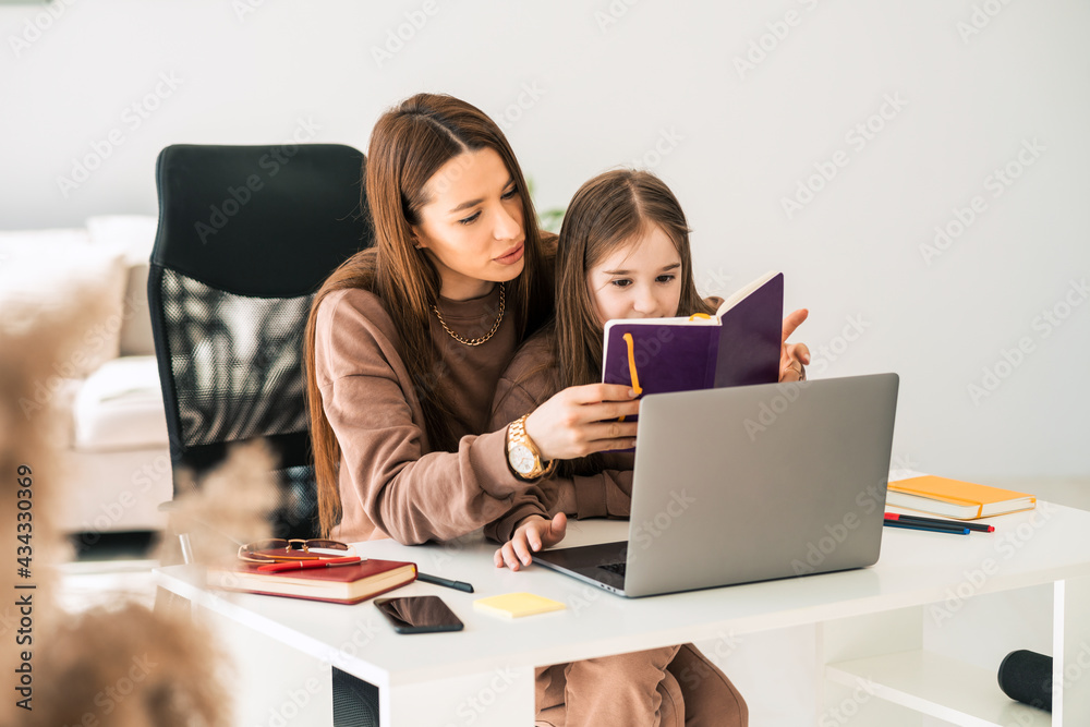 Mother and daughter are doing homework at the laptop. Little schoolgirl at the distance learning at home