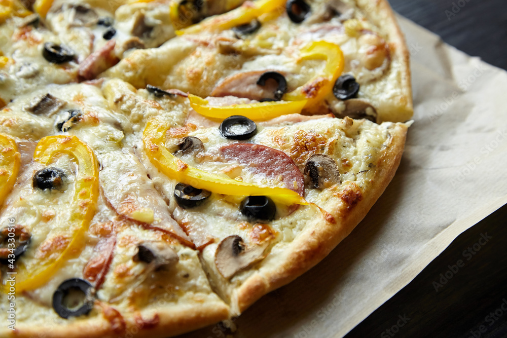Pizza with chesse, ham, yellow bell pepper, olives and mushrooms on wooden table
