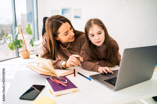 Mom and little daughter doing homework on laptop. Mother teaches the child at home