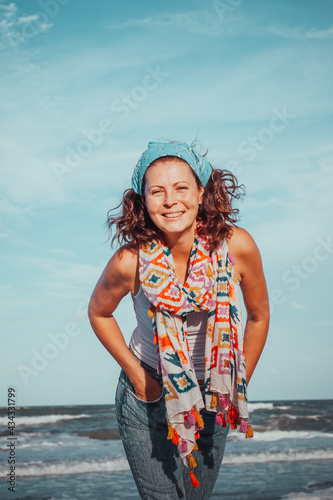 Barefoot young ethnic woman walking along on sandy beach towards the ocean during summer vacation.Portrait of charming woman enjoying beautiful seascape walking on summer day. attractive young hipster