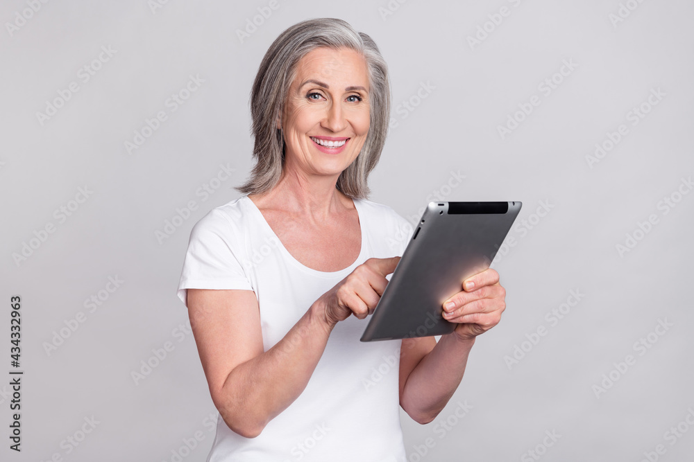 Photo of cheerful confident senior lady tape tablet wear white t-shirt isolated on grey color background