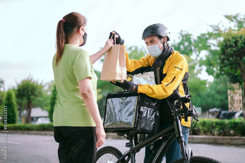 Courier wearing a yellow company shirt, riding a bicycle, delivering food paper bags to customers