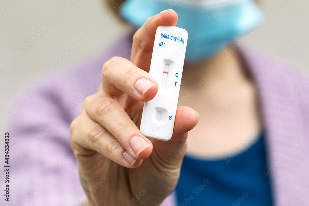 Woman in mask holds in fingers negative rapid covid test