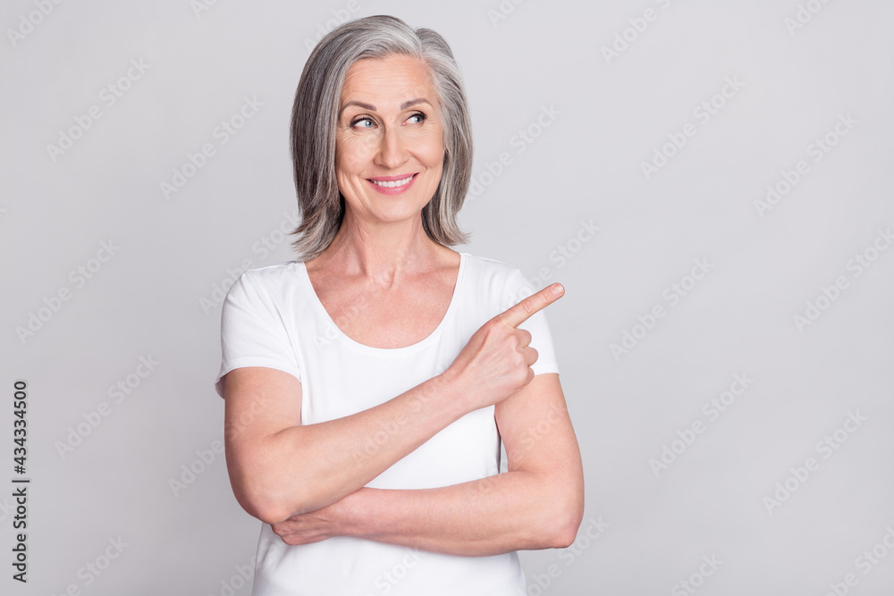 Photo of pretty adorable age woman dressed white outfit smiling looking pointing finger empty space isolated grey color background Photo of pretty adorable age woman dressed white outfit smiling looking pointing finger empty space isolated grey color background