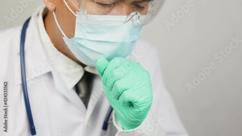 A male doctor, wearing gloves and gloves, raised his hand to cover his mouth while unraveling. The concept of working hard until sick and sick and have symptoms of pain.