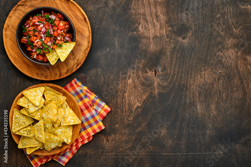 Traditional Mexican tomato sauce salsa with nachos and ingredients tomatoes, chile, garlic, onion on dark old wooden background. Concept of Latin American and Mexican food. Mock up.