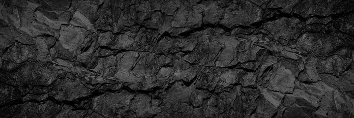 Volumetric rock texture with cracks. Black stone background with copy space for design. Wide banner.