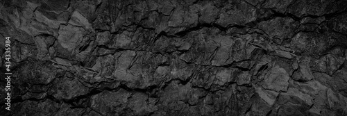 Volumetric rock texture with cracks. Black stone background with copy space for design. Wide banner.