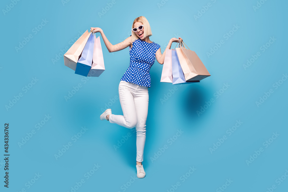 Full body photo of young girl happy positive smile shop sale black friday bags isolated over blue color background Full body photo of young girl happy positive smile shop sale black friday bags isolated over blue color background