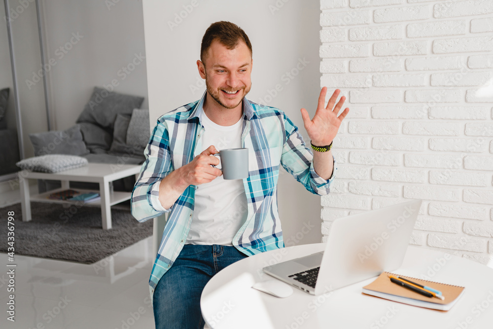 man in shirt sitting in kitchen at home at table working online on laptop man in shirt sitting in kitchen at home at table working online on laptop
