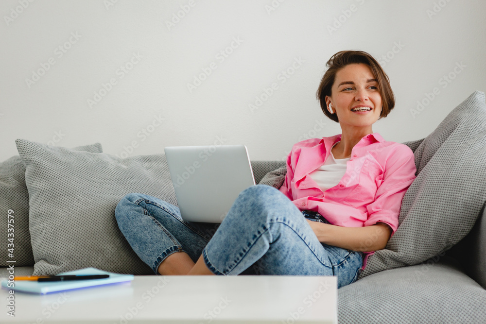 woman in pink shirt sitting relaxed on sofa at home at table working online on laptop woman in pink shirt sitting relaxed on sofa at home at table working online on laptop