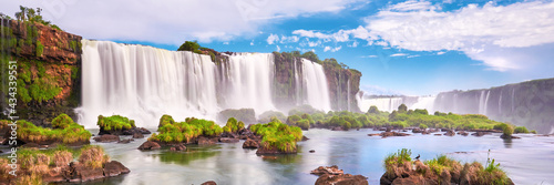 Iguazu waterfalls in Argentina. Panoramic view of many majestic powerful water cascades with mist and clouds. Panoramic image of Iguazu valley with grass and stones in calm water. photo