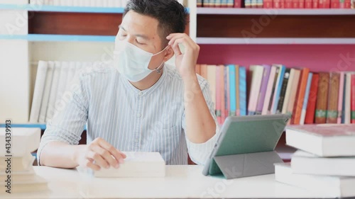 A young Asian man wearing a mask in his office is sitting blankly out of the window, exhausted, spaced out, and confined to work at home.