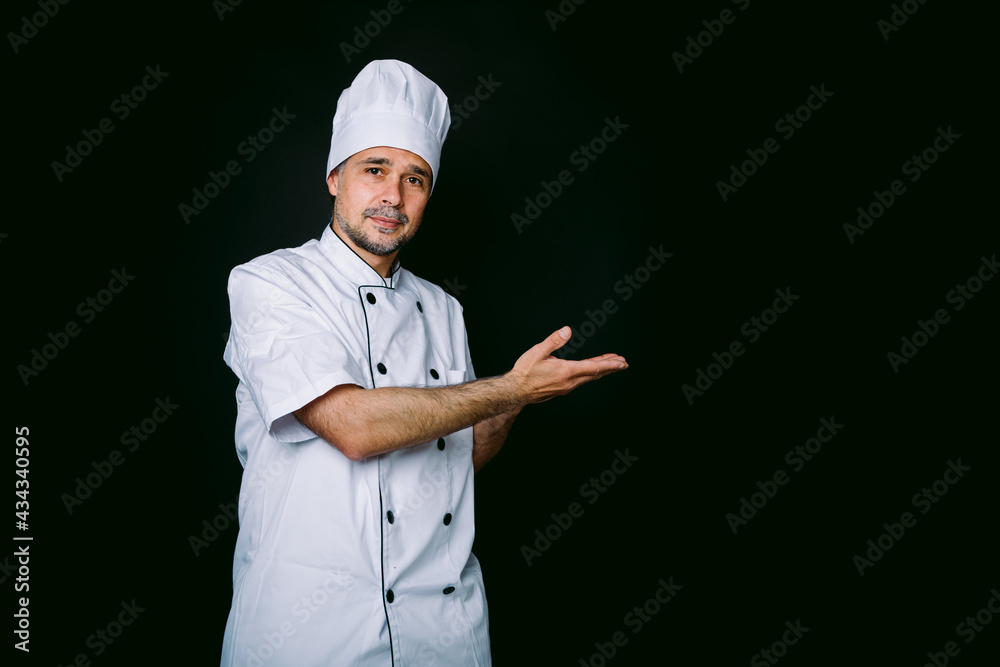 Chef cook wearing jacket and kitchen hat pointing right on black background Chef cook wearing jacket and kitchen hat pointing right on black background