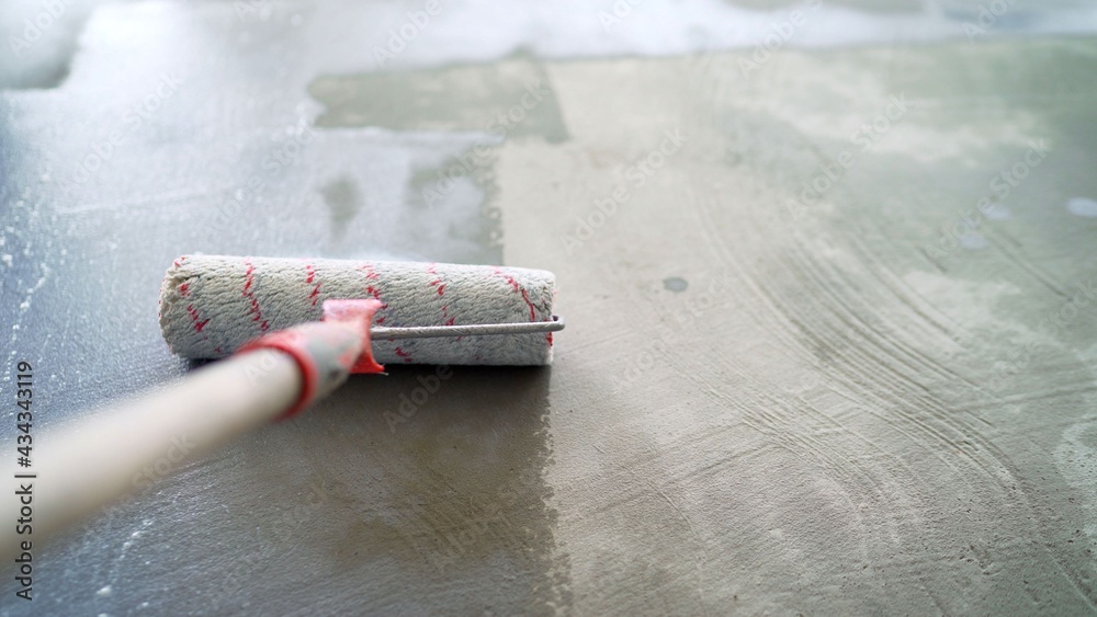 Priming the floor in a large room. worker is preparing the floor with