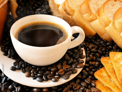 Hot coffee in a white cup and crackers and breads and lots of coffee beans