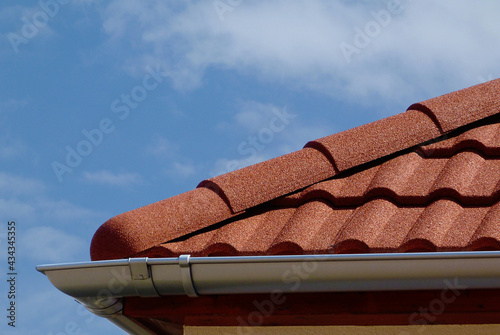 half round ridge tiles and shallow zink gutter in grey silver color. textured modern concrete tile roof. closeup detail. house construction concept. light blue sky background
