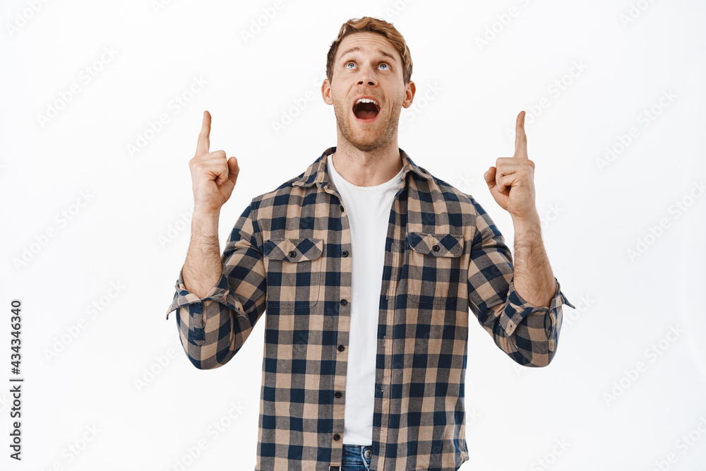Wow look at this. Impressed and excited redhead caucasian male, pointing fingers up, looking above with fascinated amazed face, checking out new promo offer, standing over white background Wow look at this. Impressed and excited redhead caucasian male, pointing fingers up, looking above with fascinated amazed face, checking out new promo offer, standing over white background