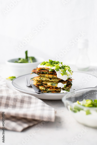Potato pancakes with spinach  garlic and green onions served with sour cream dip on a plate on a light background 