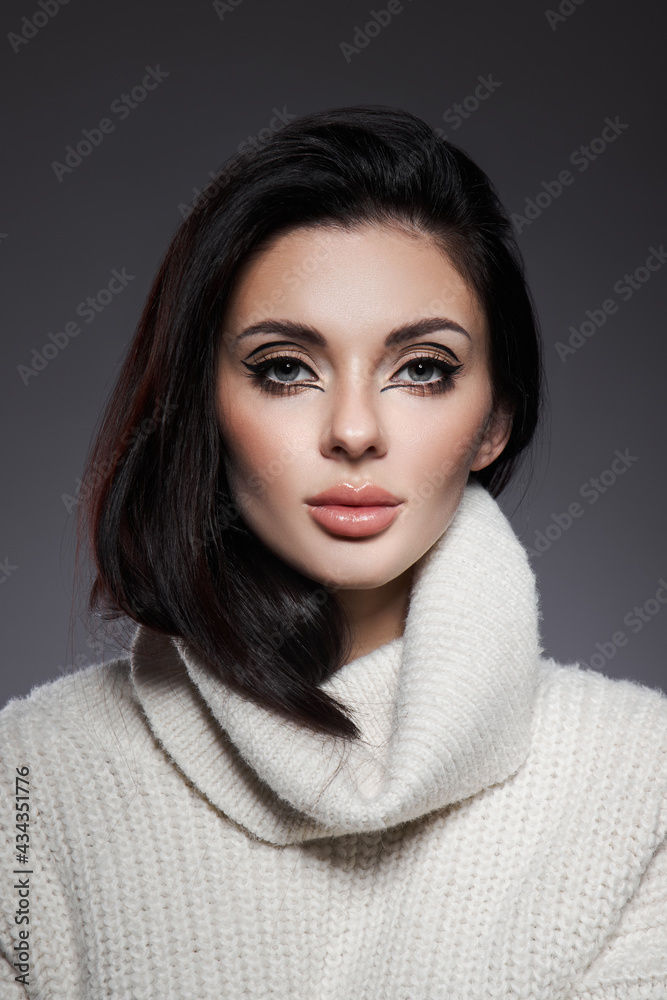 Beauty portrait of woman in white sweater, perfect evening makeup on dark background. Perfect skin without wrinkles, professional beauty makeup, long black hair