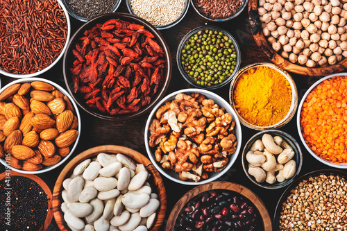 Superfoods, legumes, cereals, nuts, seeds set in bowls on wooden background. Superfood as chia, spirulina, beans, goji berries, quinoa, turmeric and other. Top view