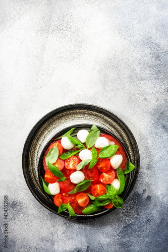Summer caprese salad with red tomatoes and white mozzarella cheese with fresh green basil leaves. Gray table. Top view