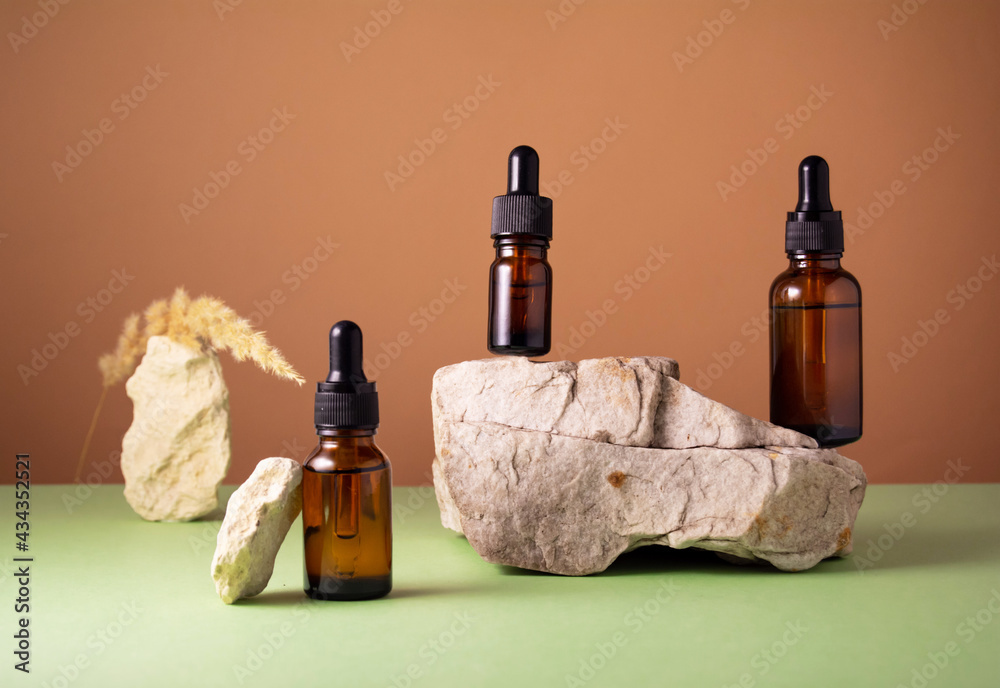 Naklejka premium Serum and oil cosmetic bottles on concrete stone podium with dry spikelet on brown and green background. Trendy natural organic healthy hair, face and body skin care