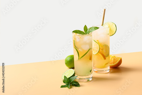 Two summer cold mojito cocktails with orange and lime slices on color white and beige background. Refreshing summer beverage.
