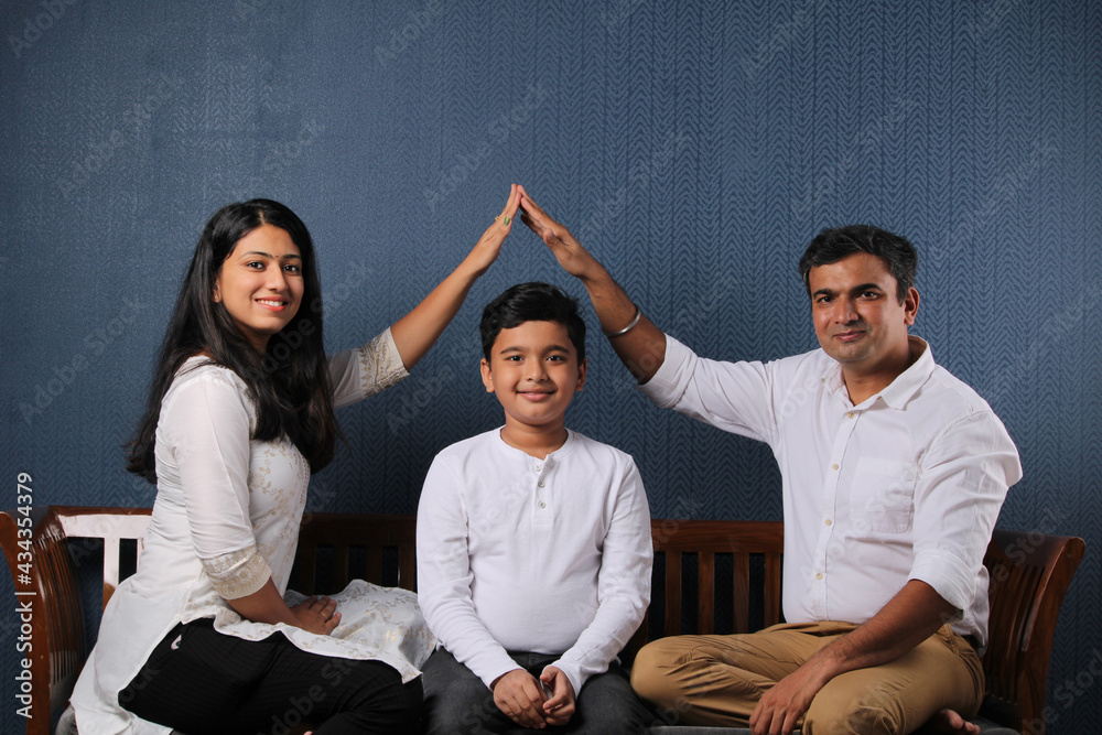 Happy indian couple with single child making roof with hands symbol of ...