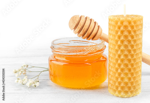 Bild auf Leinwand Glass jar with honey, beeswax candle, honey dipper and white flower on a wooden table against white background, front view, close-up, copy space